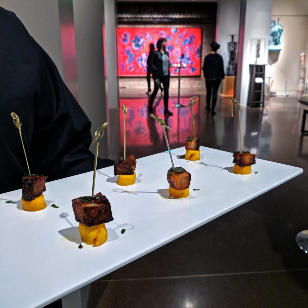 hors d'oeuvres on a white serving tray in the foreground, with people in front of a Kirkland dot painting in the galleries behind.